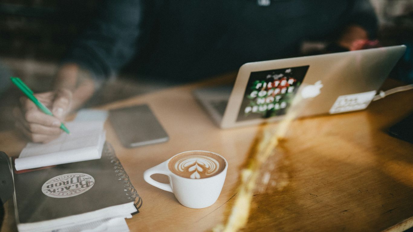 cappuccino art on white ceramic mug beside MacBook Air