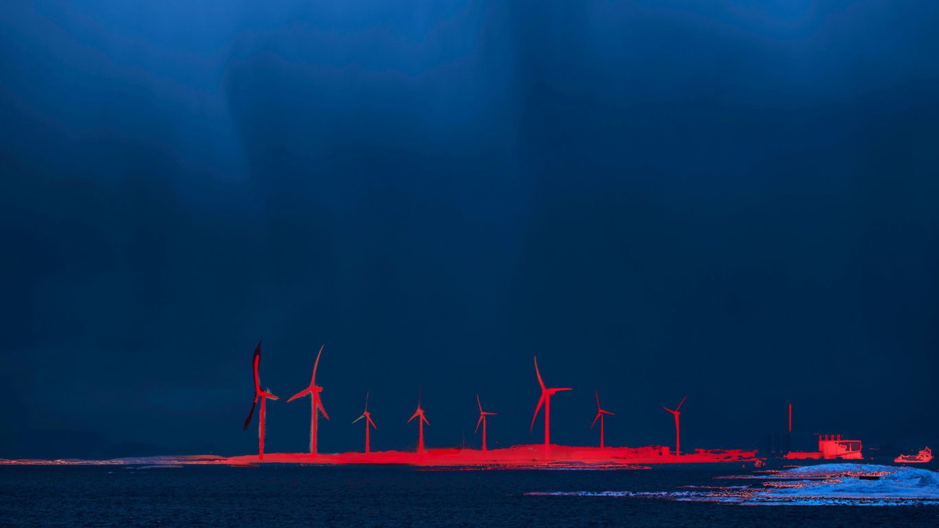 Wind turbines illuminated red at dusk over water.