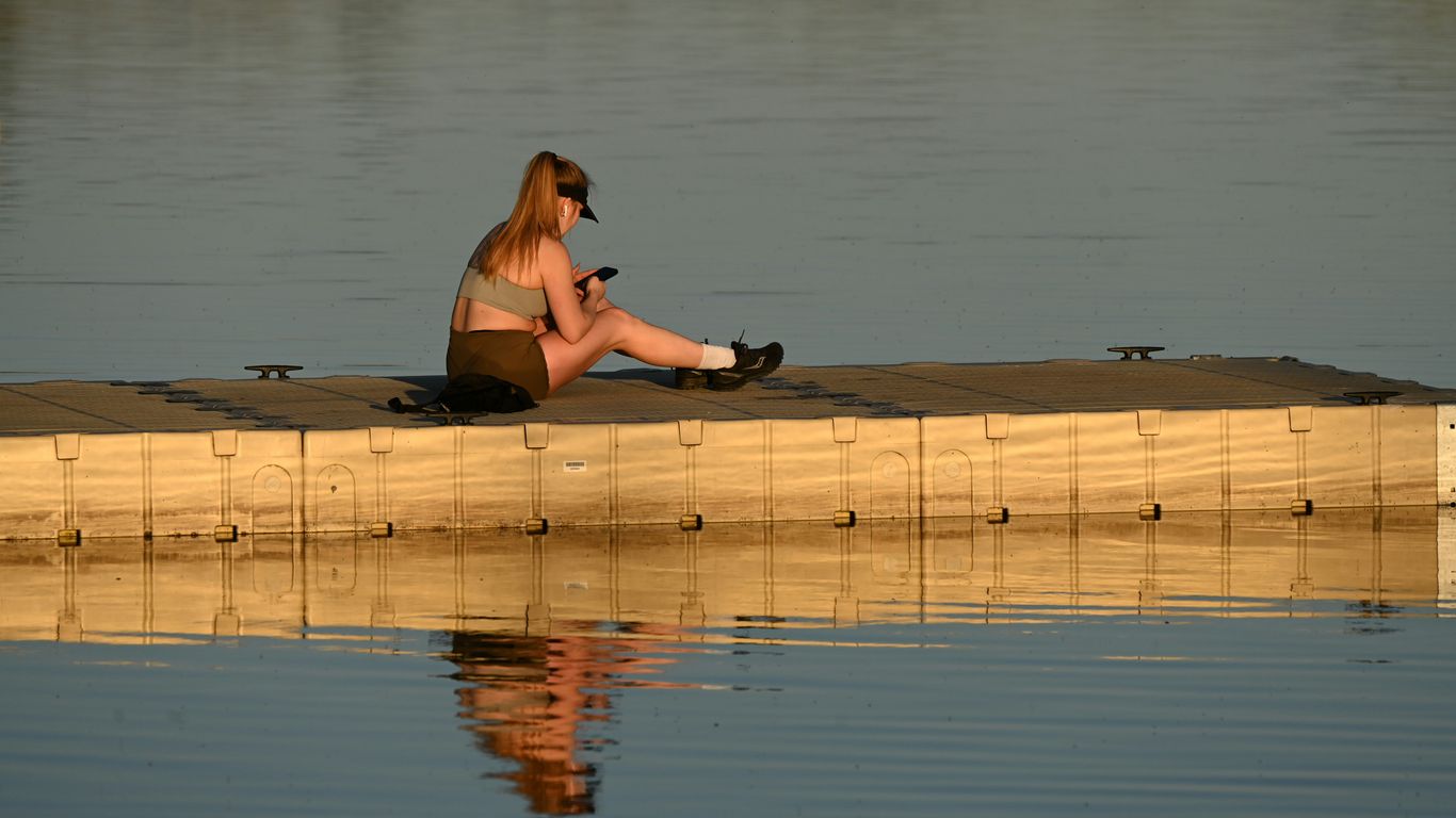 Woman sitting and looking at her phone by the water.