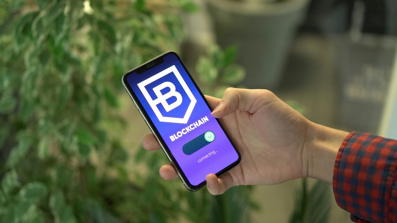 A hand holding a smartphone displaying a blockchain app.