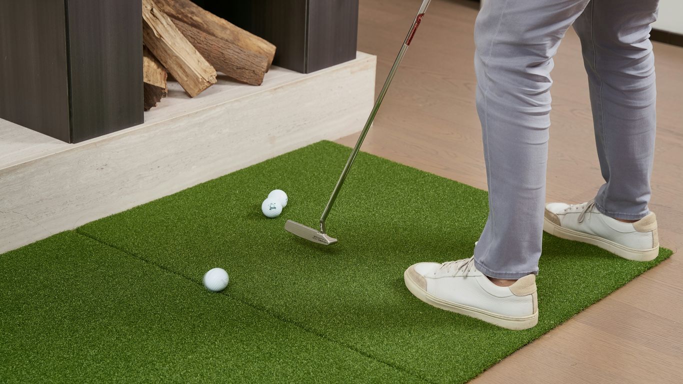 Person practicing golf putt on indoor putting green.