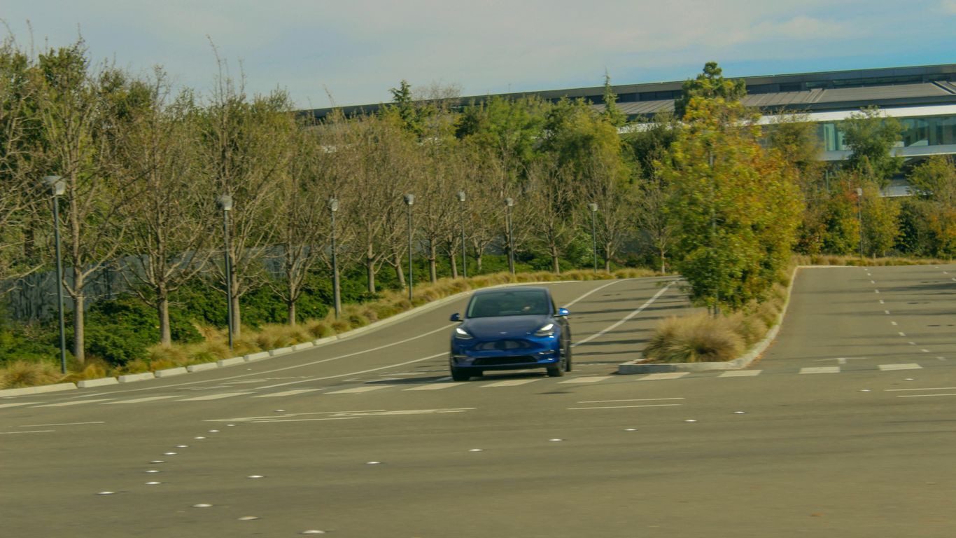 a blue car driving down a street next to trees