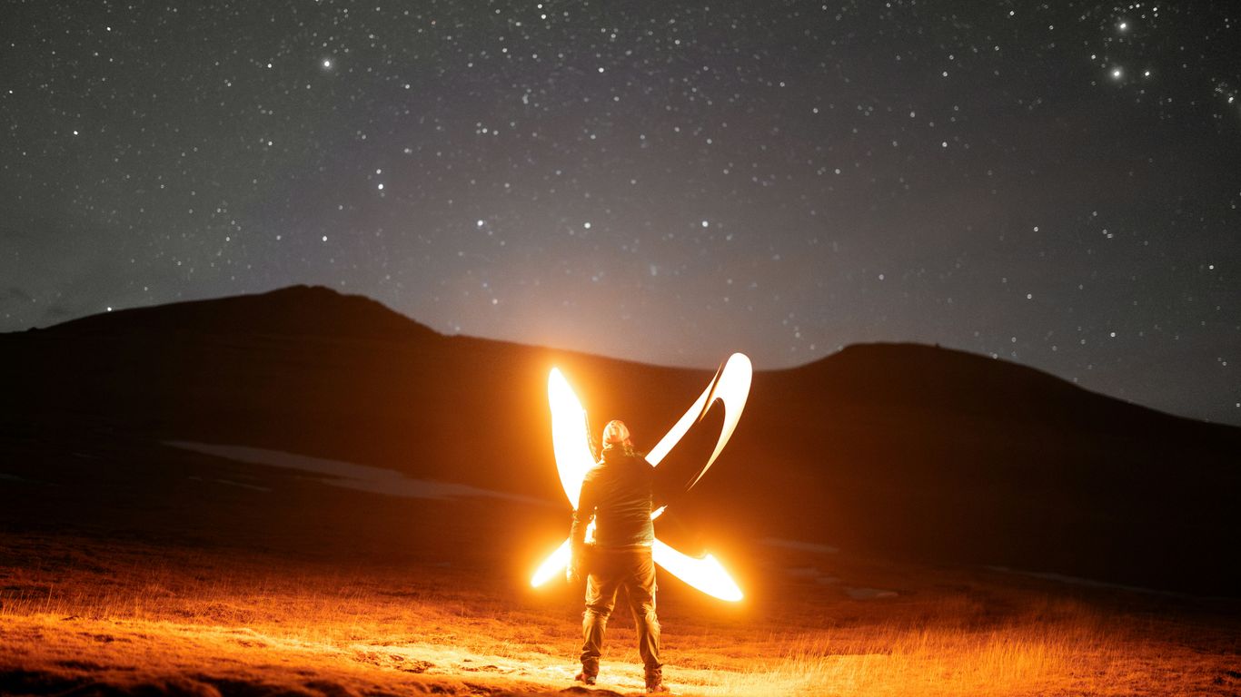A man standing in the middle of a field holding a fire
