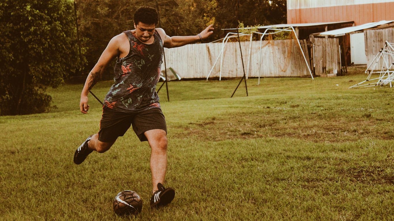 man kicking football on grass field during daytime