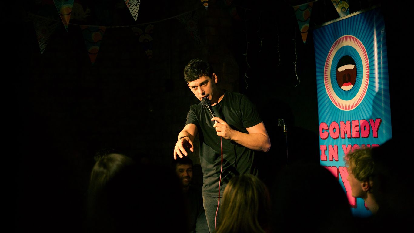 A comedian performs on stage with a banner that says "Comedy in Your".