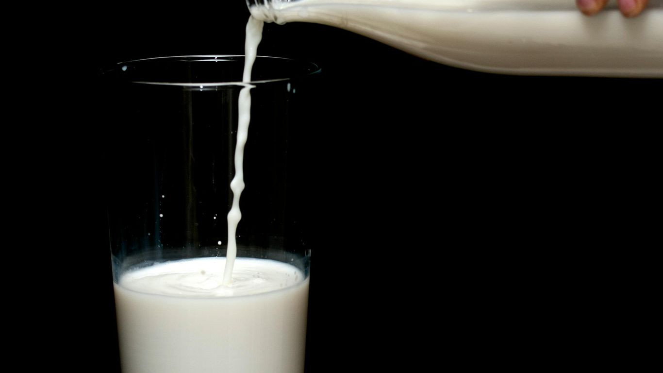 Milk being poured from a bottle into a glass, black background.