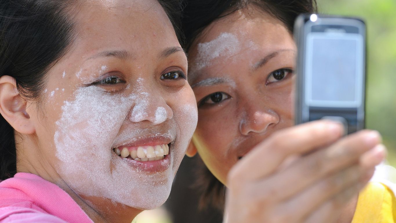 Two women take a selfie, faces with white substance.