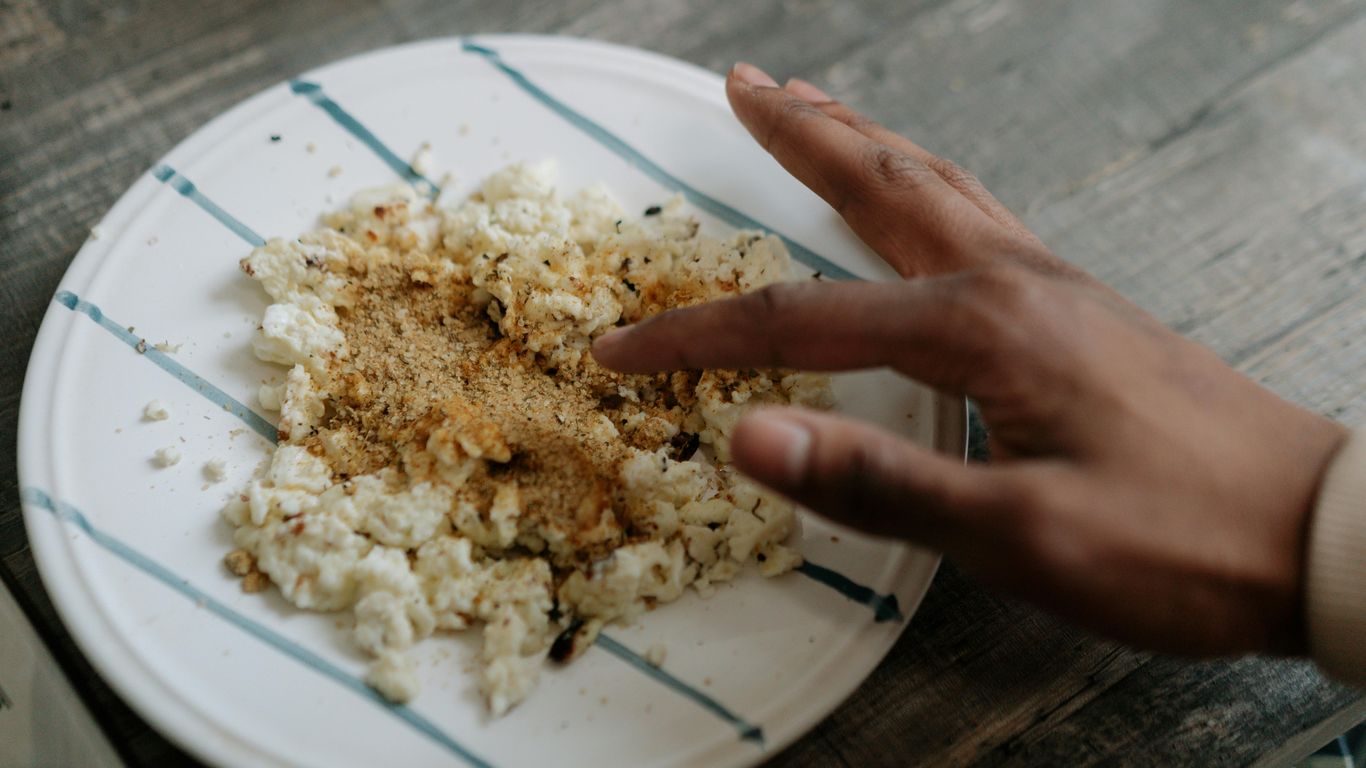 Hand reaching for food on a plate with crumbled topping.
