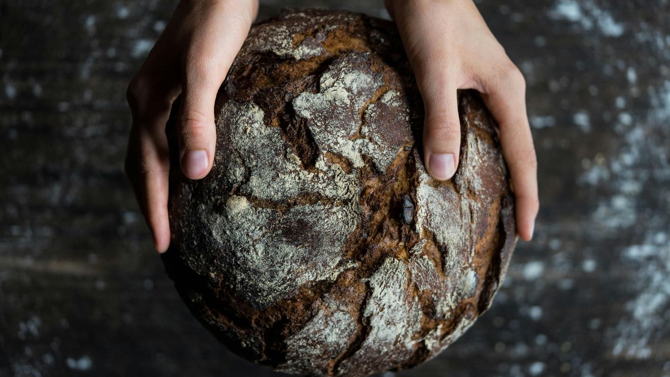 Two hands holding a rustic round loaf of bread.