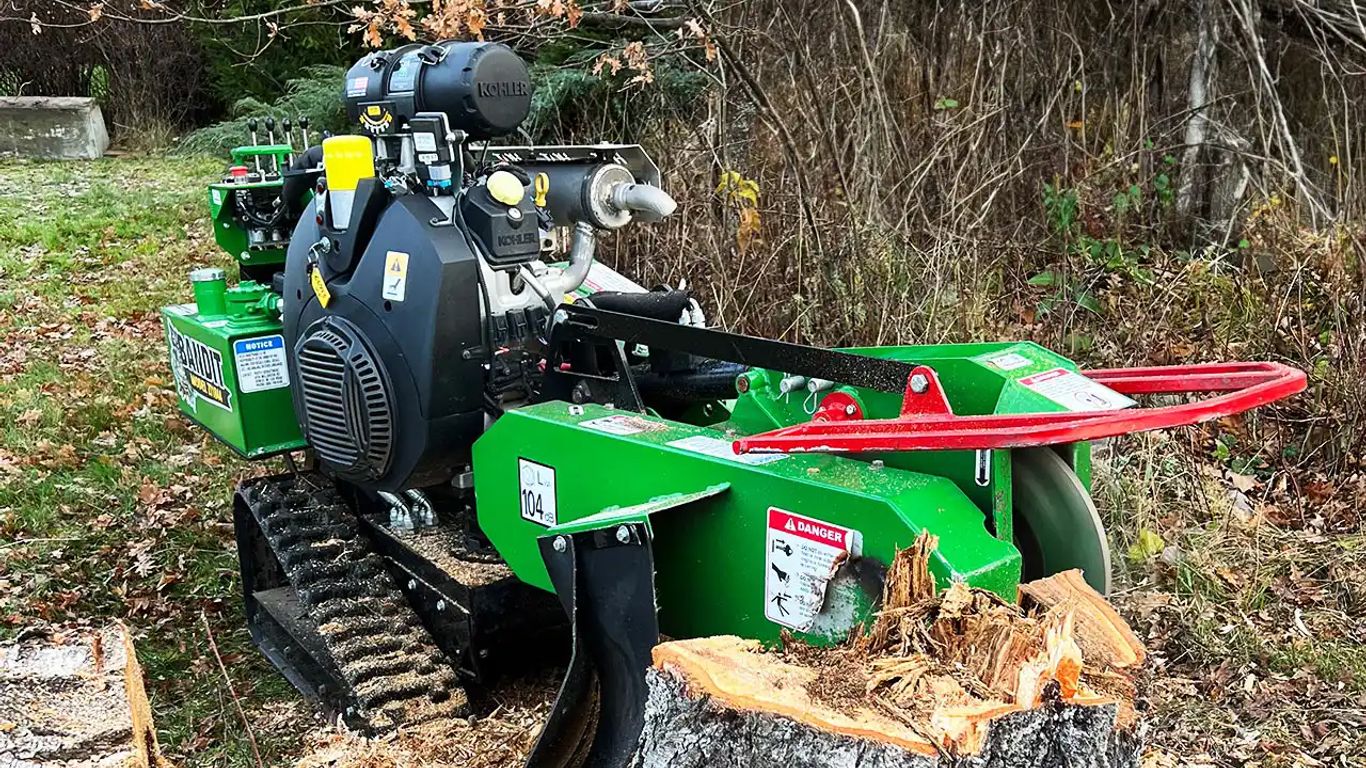 A green stump grinder with tracks in a forested area.