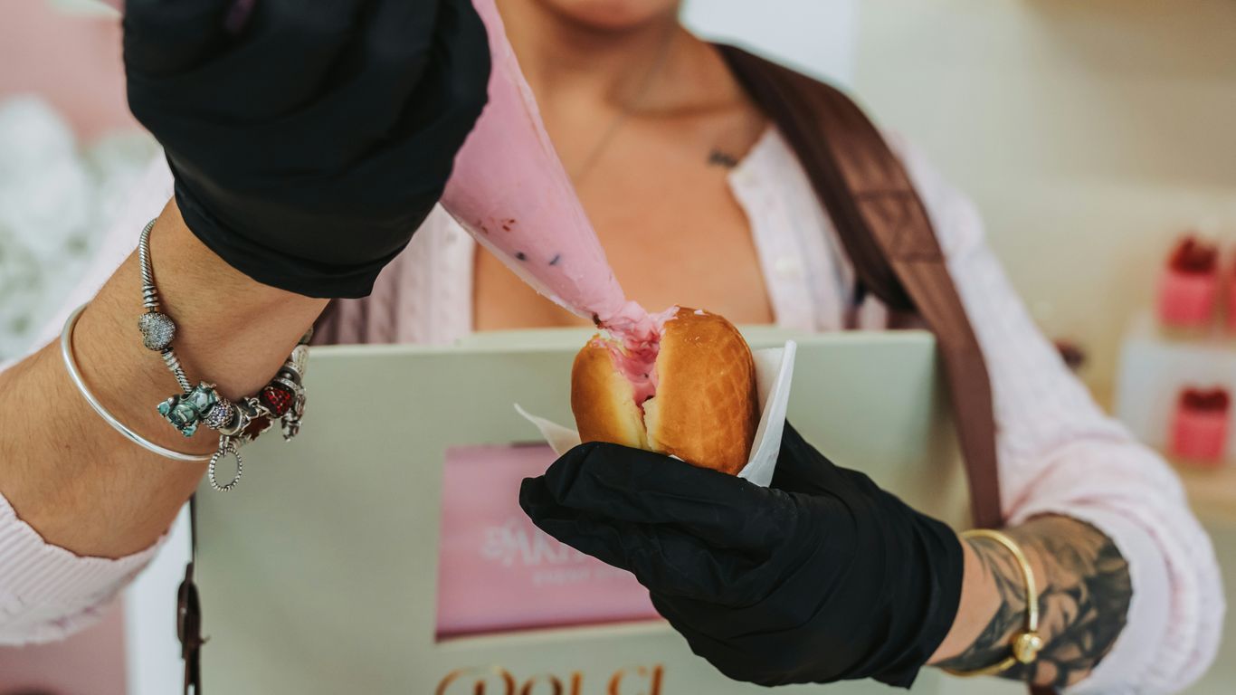 Baker decorates pastry with pink frosting using a piping bag.