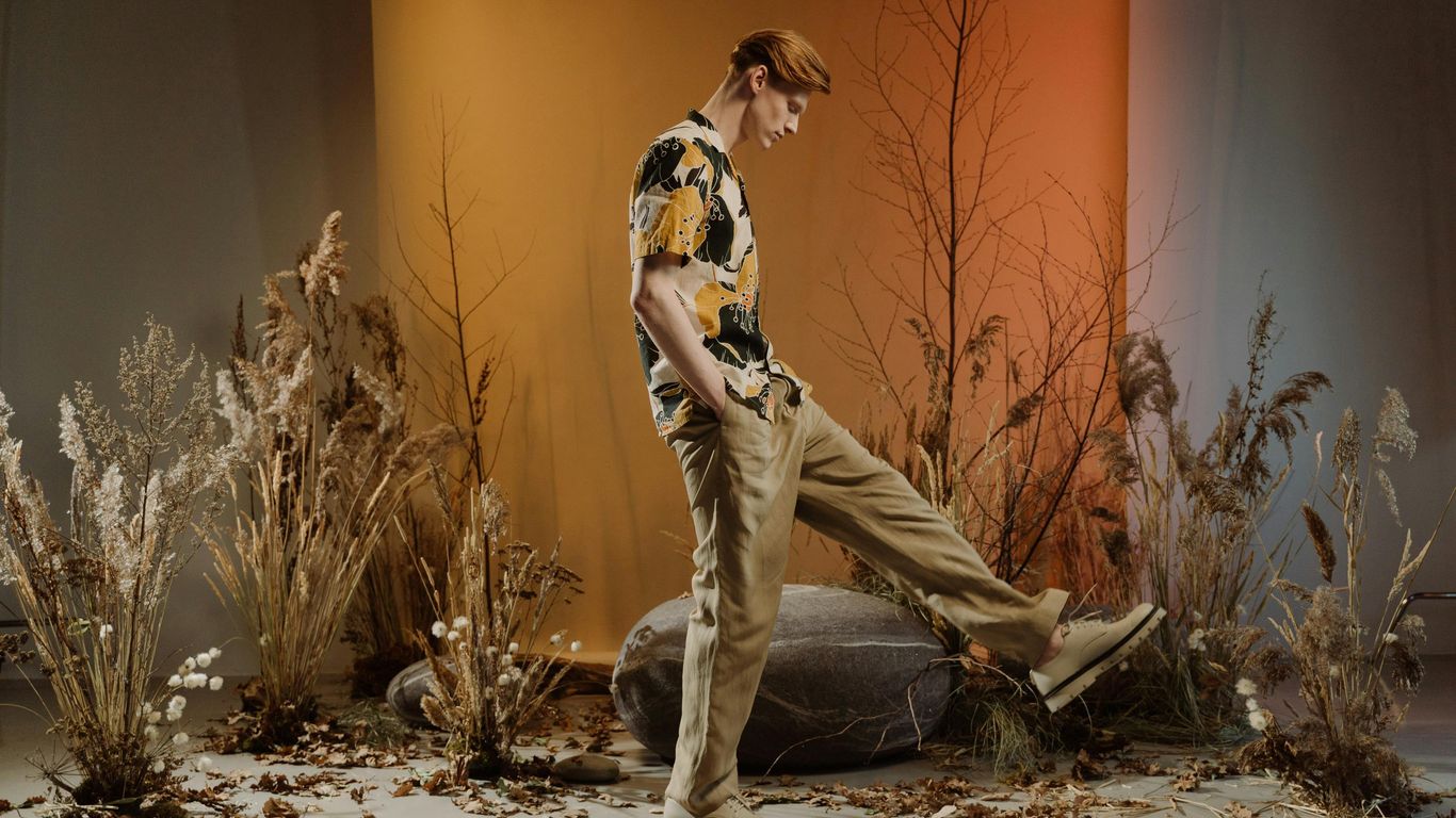 Person standing among dry plants, autumn leaves, and warm lighting.