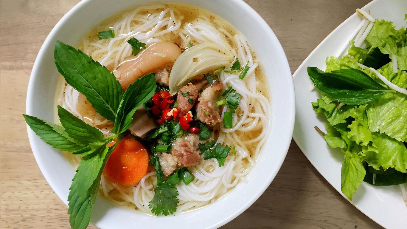 Bowl of noodle soup with herbs, vegetables, and fresh greens.