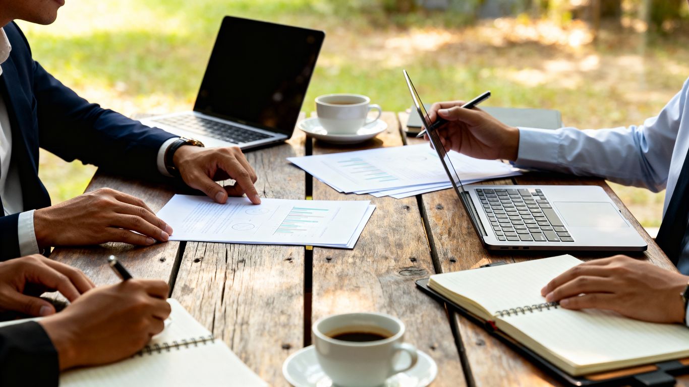 Business meeting outdoors with laptops, papers, and coffee.