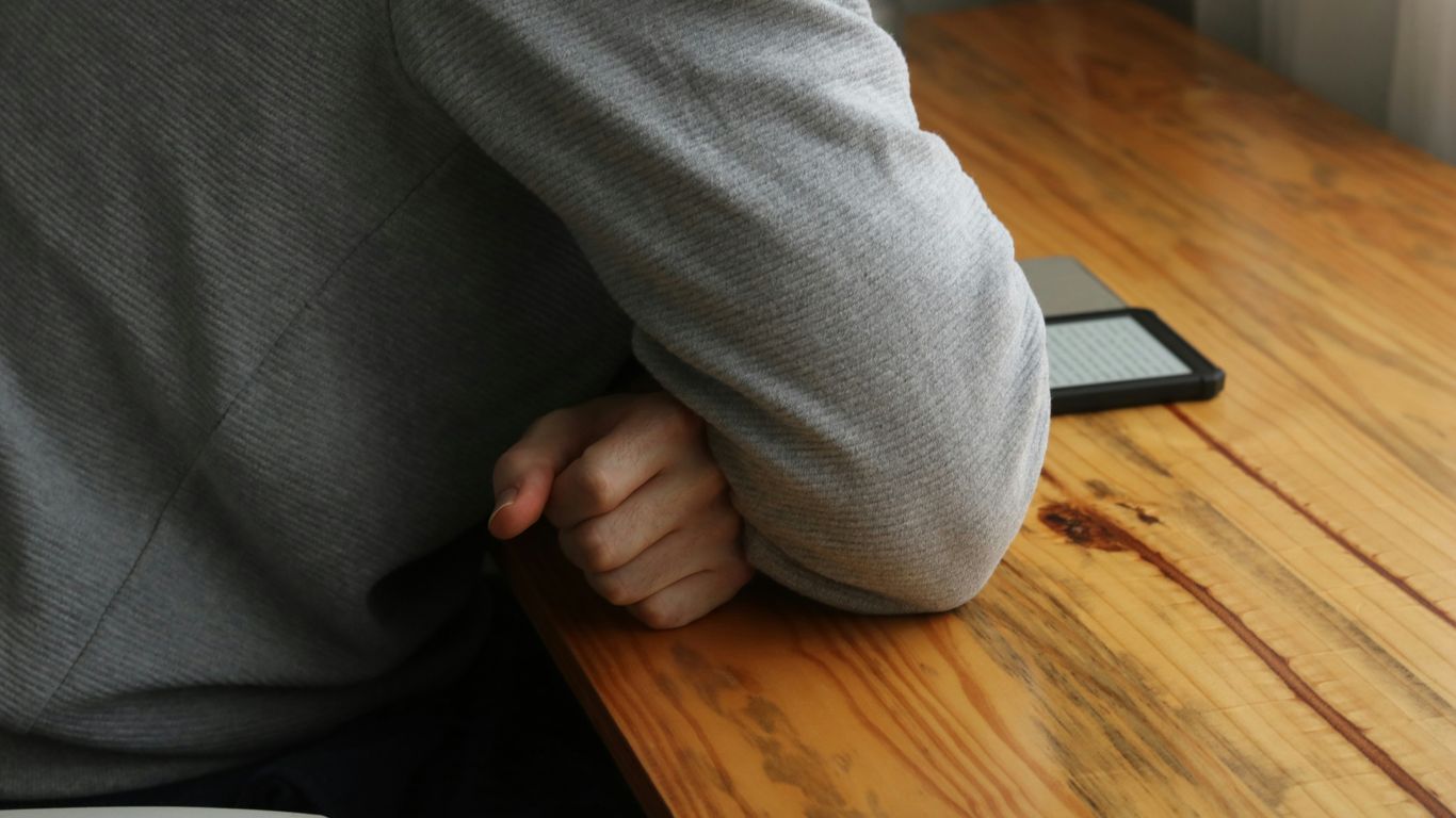 Person leans on a wooden table with their elbow.