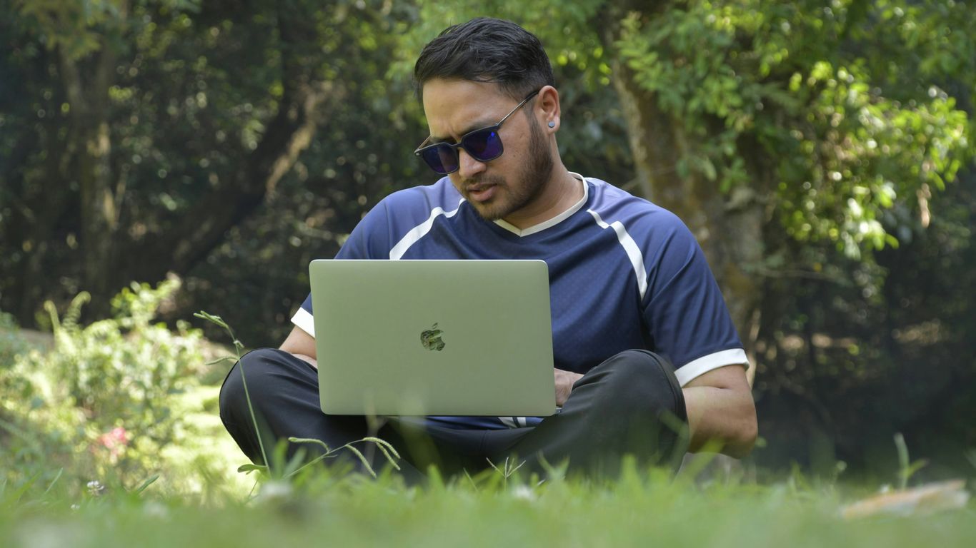 a man sitting in the grass using a laptop computer