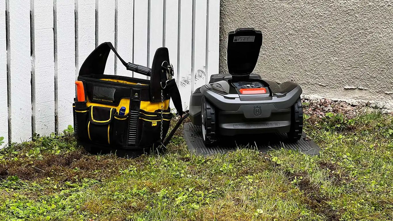 A tool bag next to a robotic lawn mower on grass.