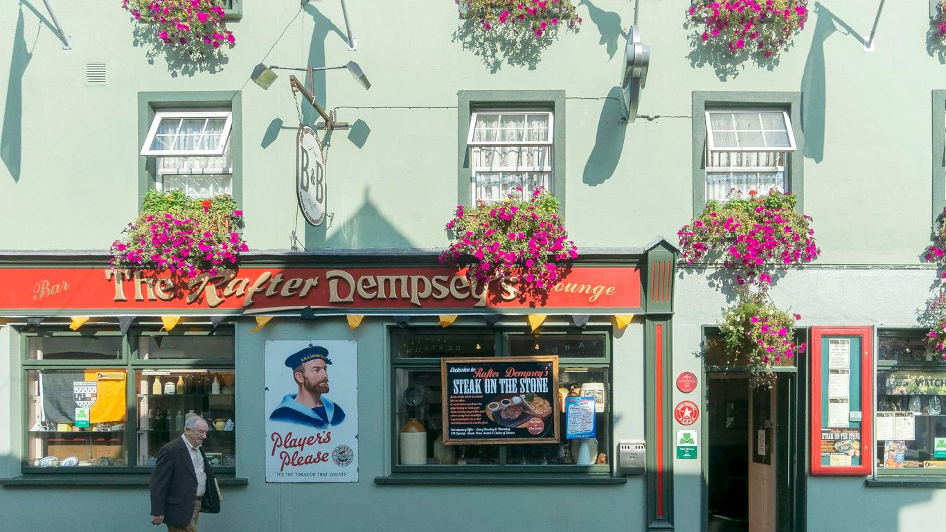 Irish pub with hanging flowers and a passerby.