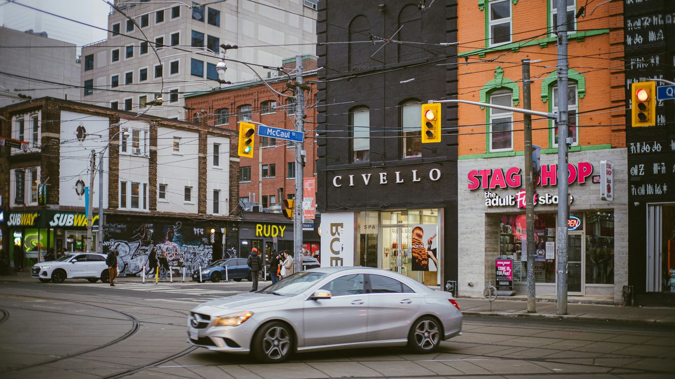 A silver car driving down a street next to tall buildings