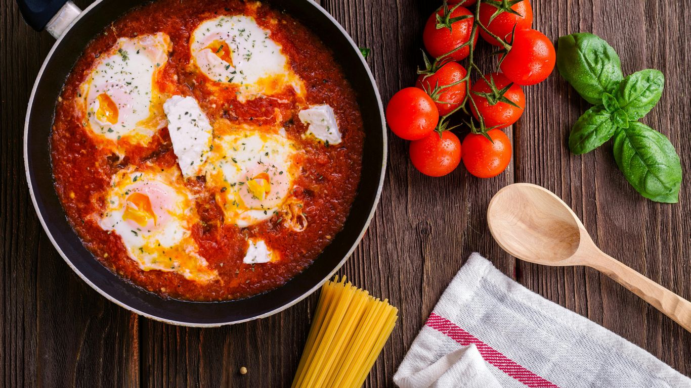 Eggs in tomato sauce, fresh tomatoes, basil, pasta, wooden spoon.