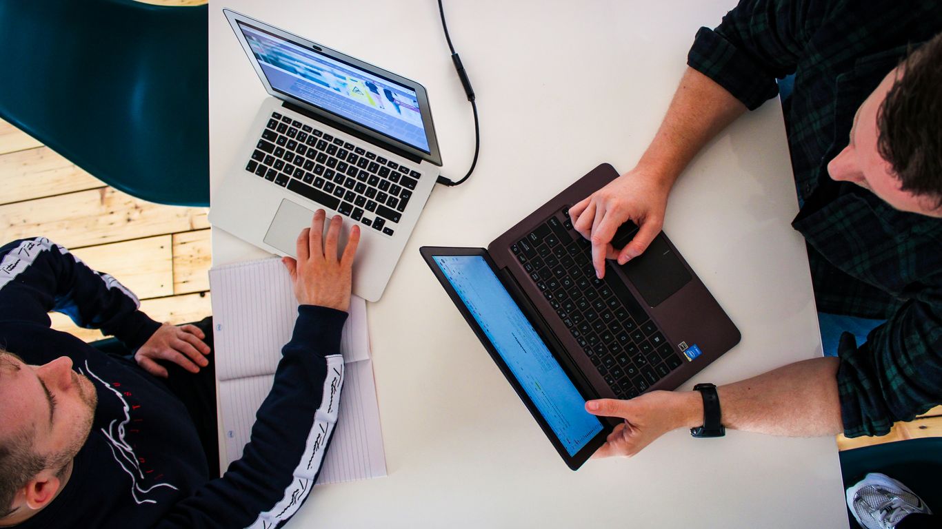 two men sitting at a table working on laptops