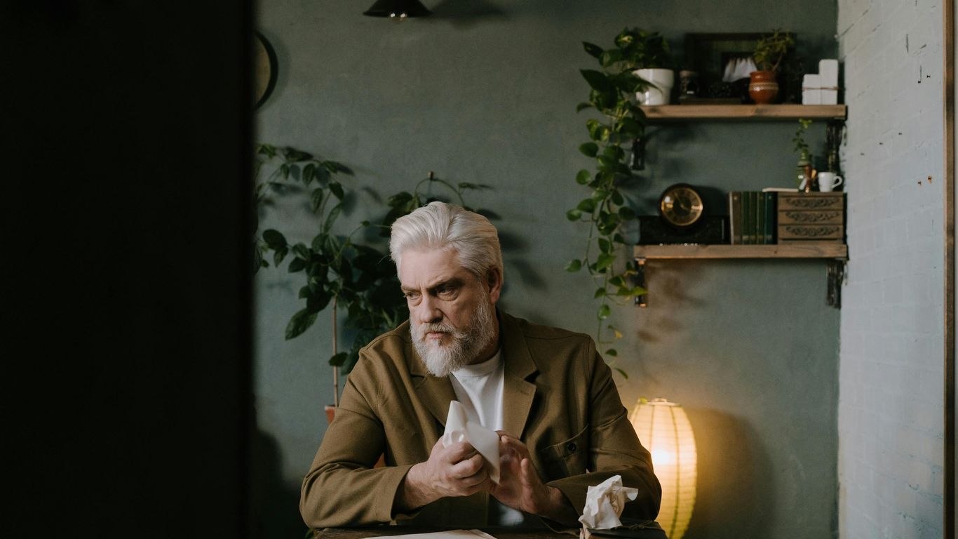 Person sitting at desk, holding tissue, surrounded by plants.