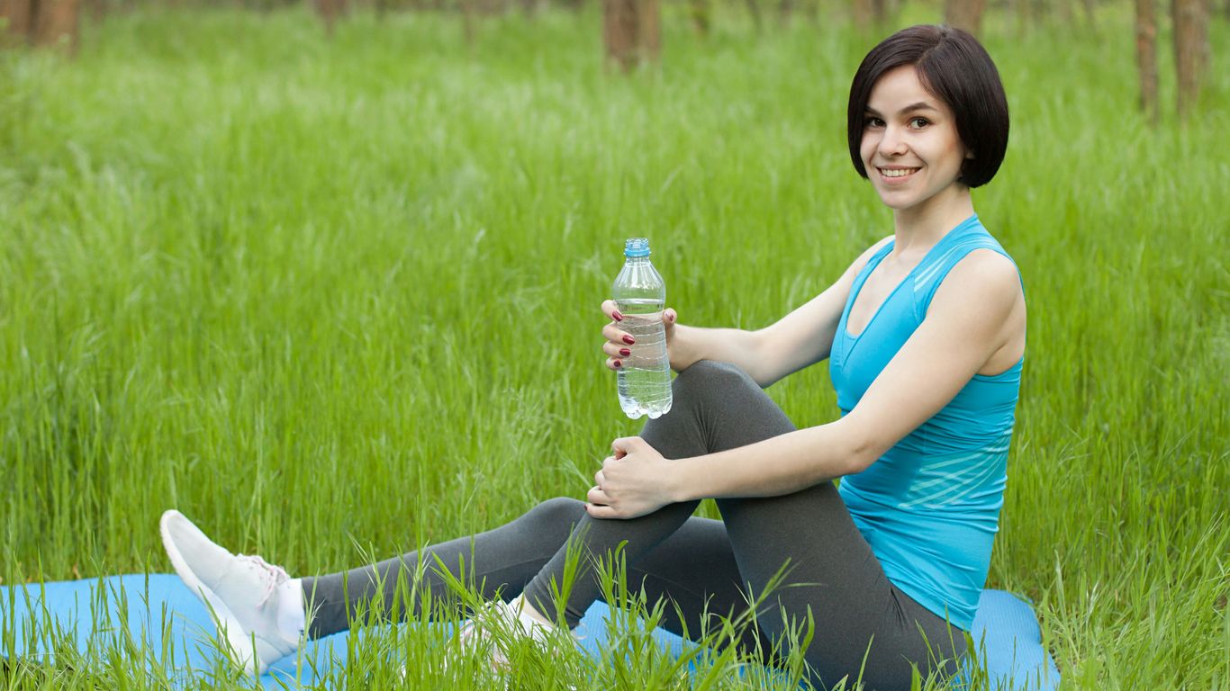 woman in blue tank top and black pants sitting on green grass field