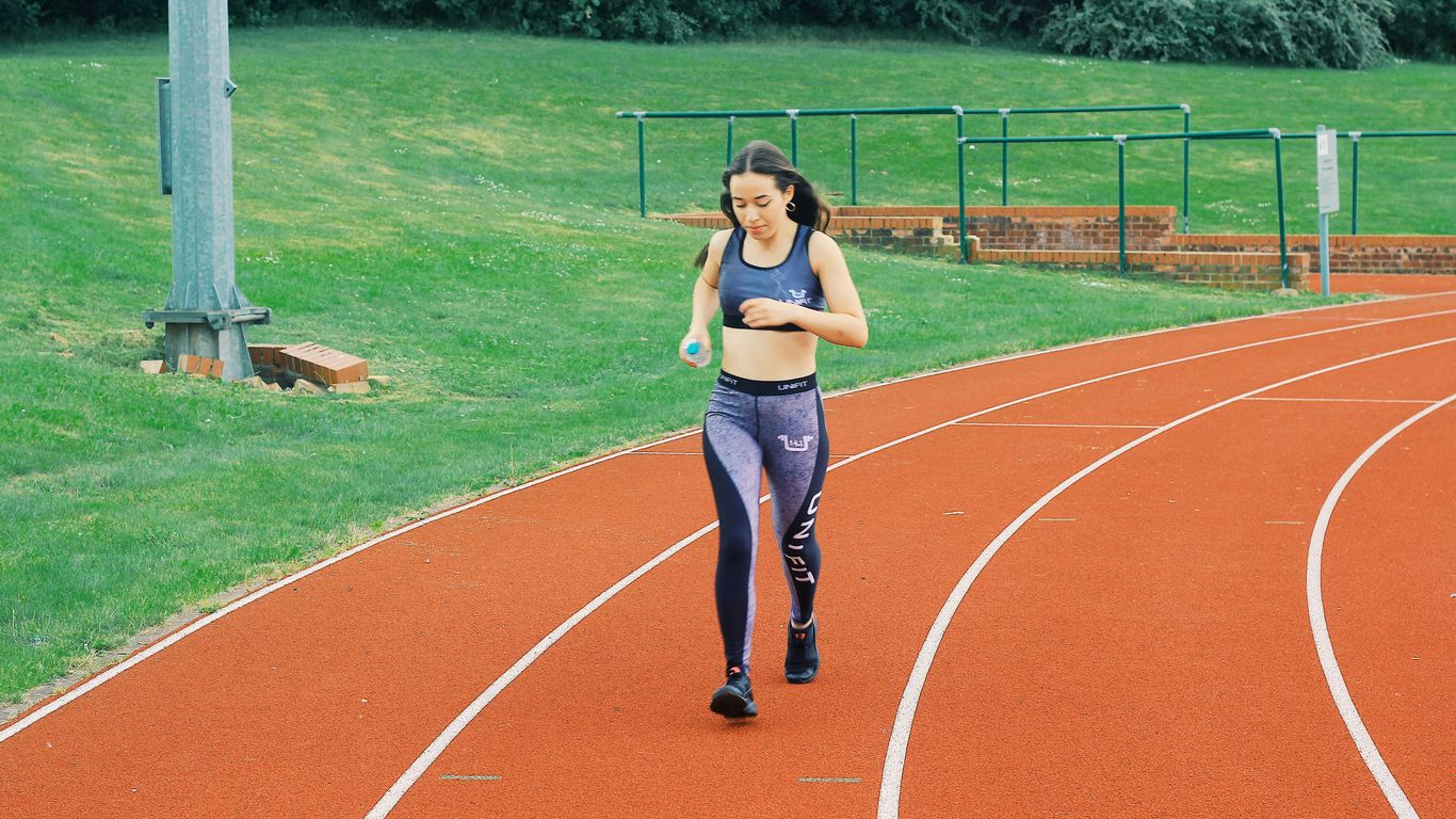 woman in black sports bra and blue denim jeans standing on track field during daytime