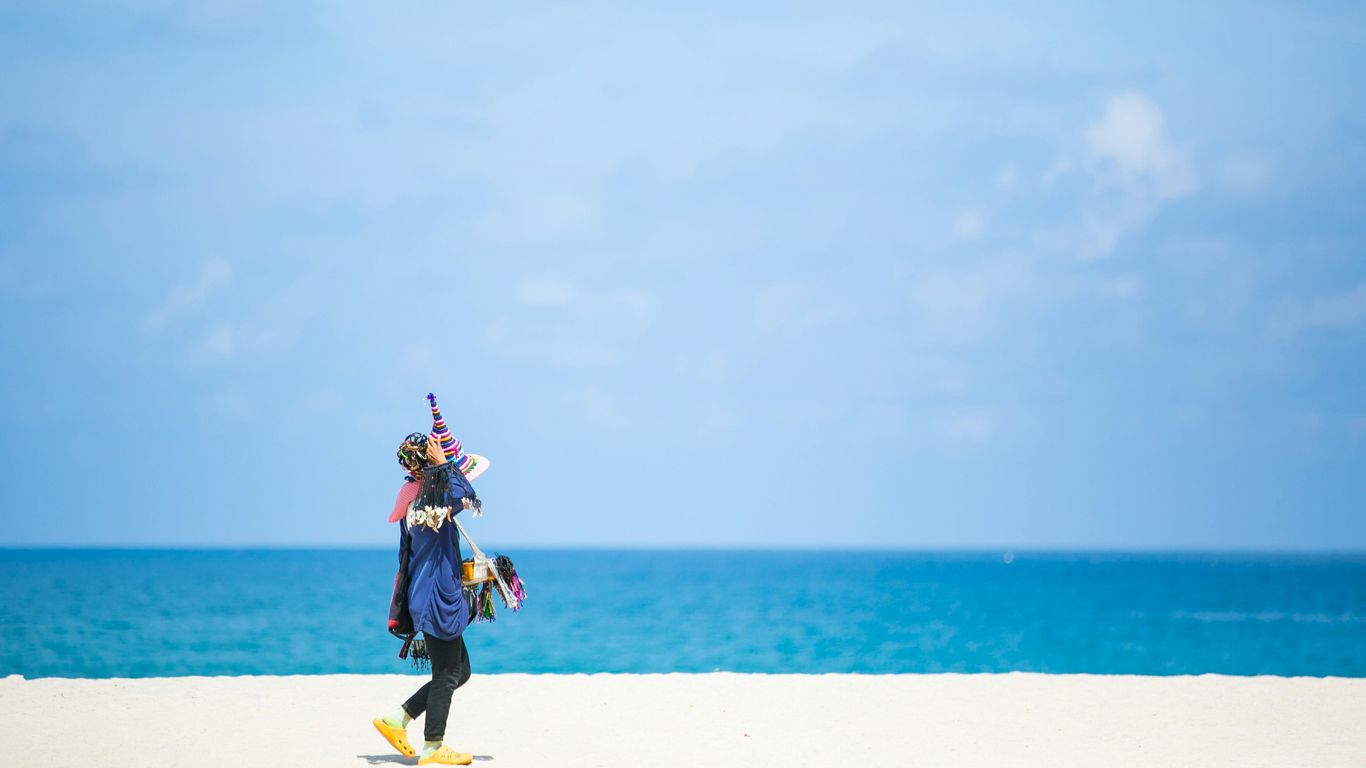 woman in blue and yellow dress walking on white sand beach during daytime