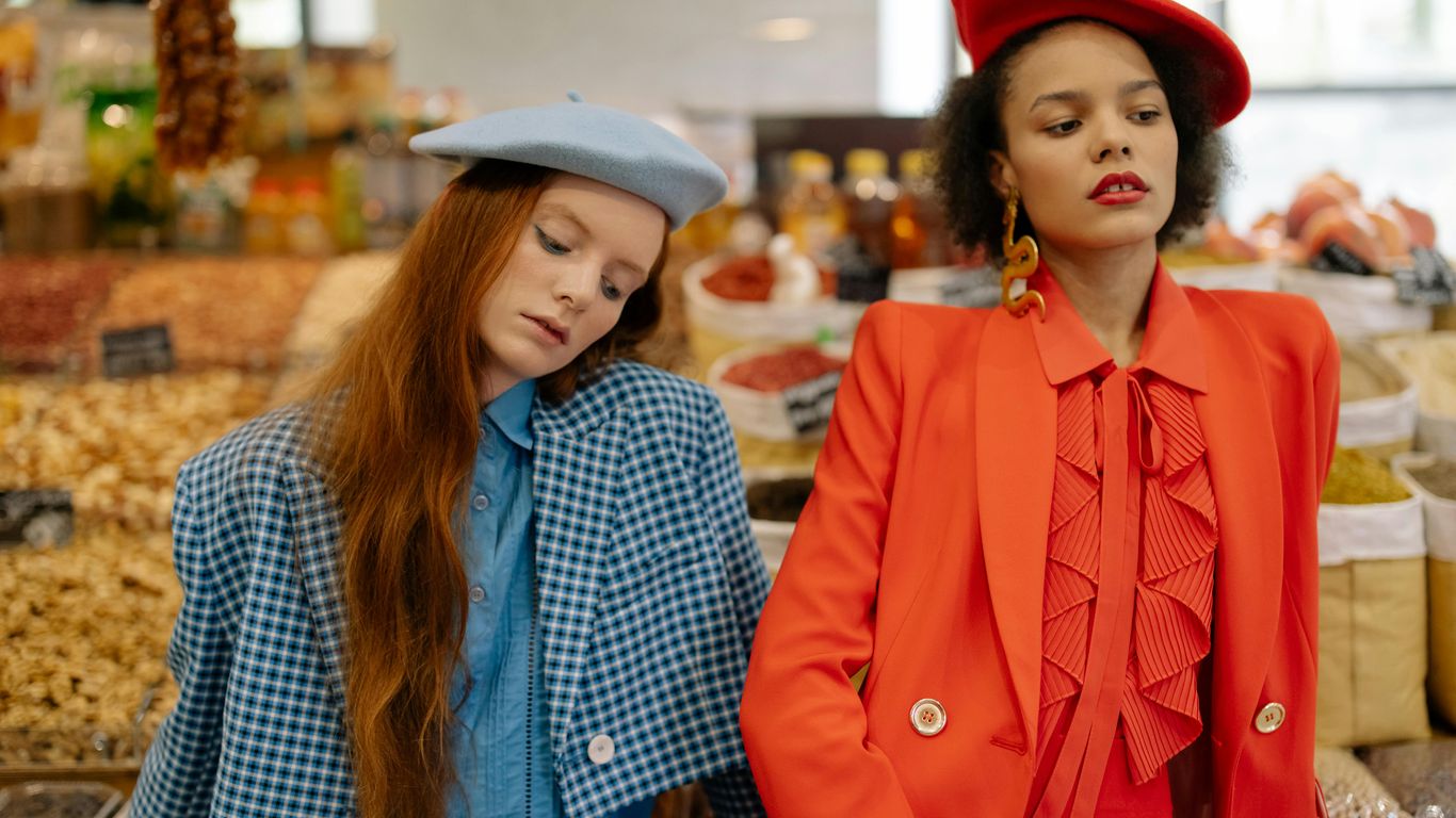 Two stylish people in a market with colorful spices and nuts.