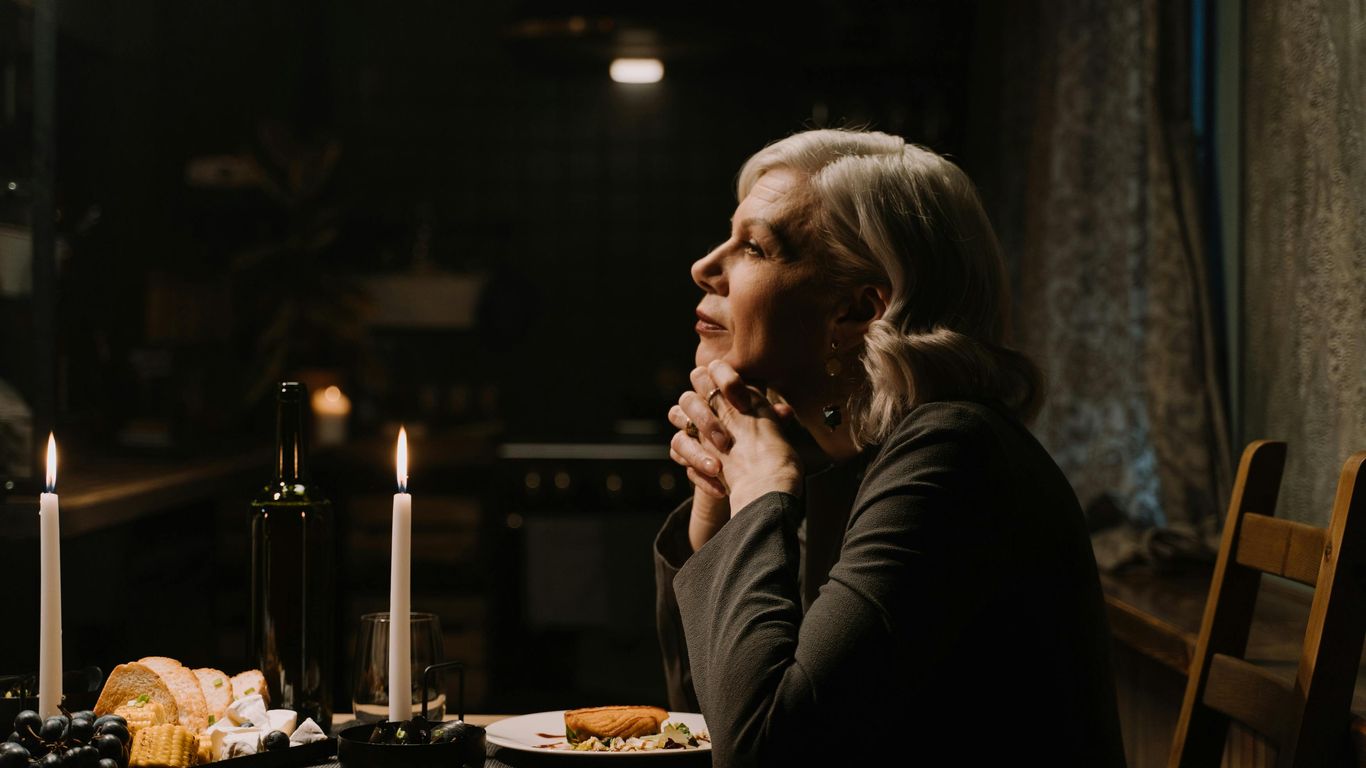 Person sitting at candlelit dinner table, appearing thoughtful and serene.