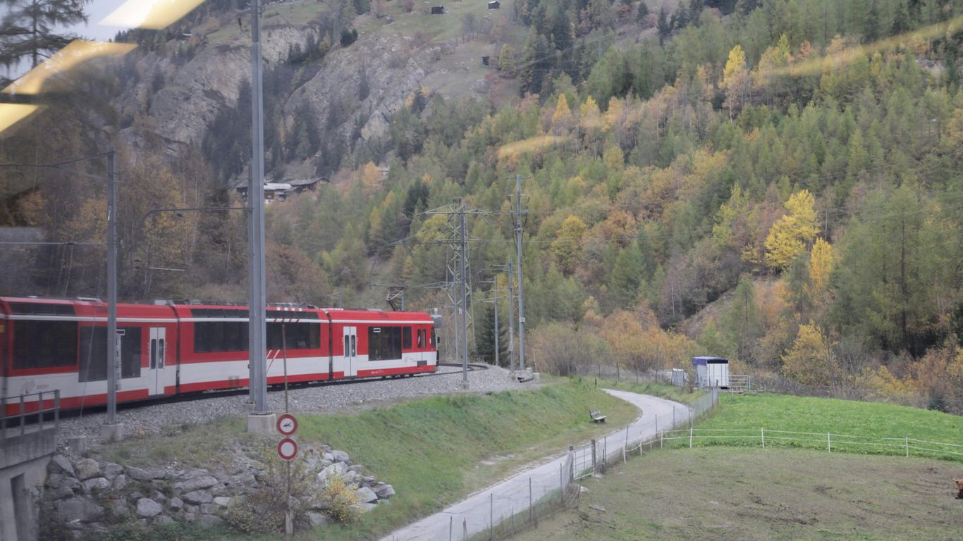 a red train traveling past a lush green hillside