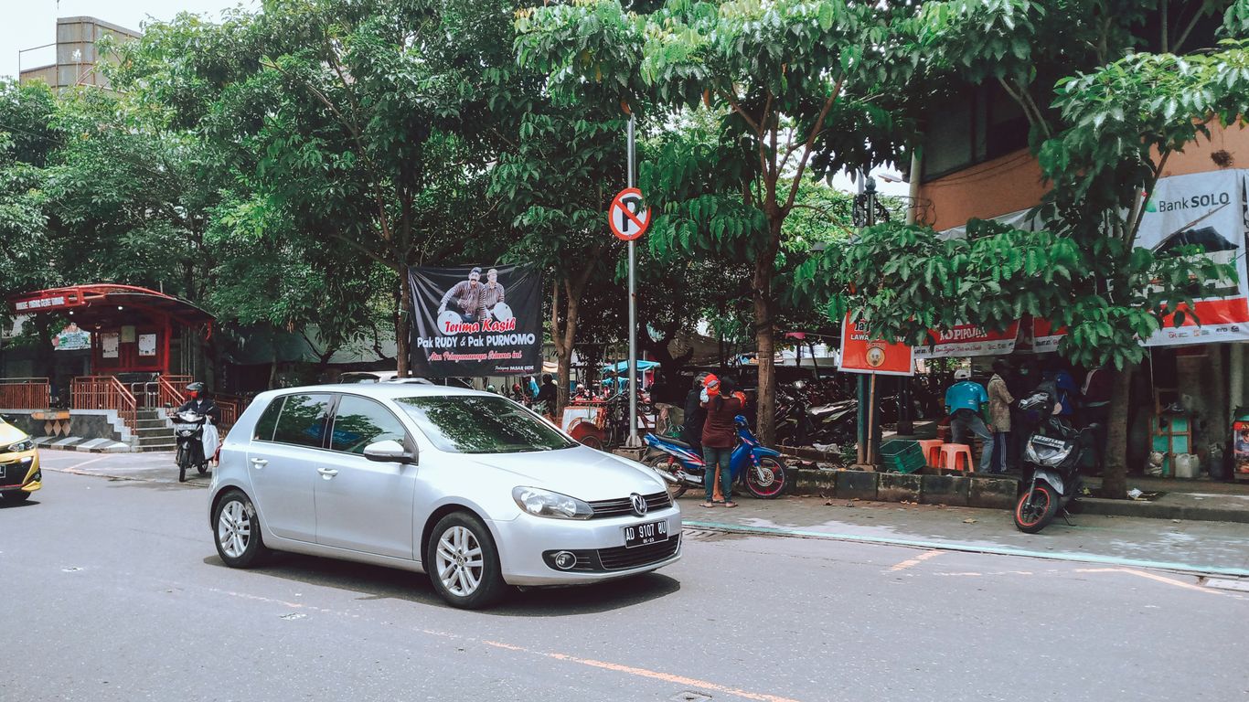 a silver car driving down a street next to trees