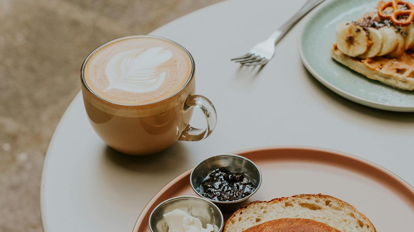 Bagel with cream cheese, jam, latte, and waffle breakfast.