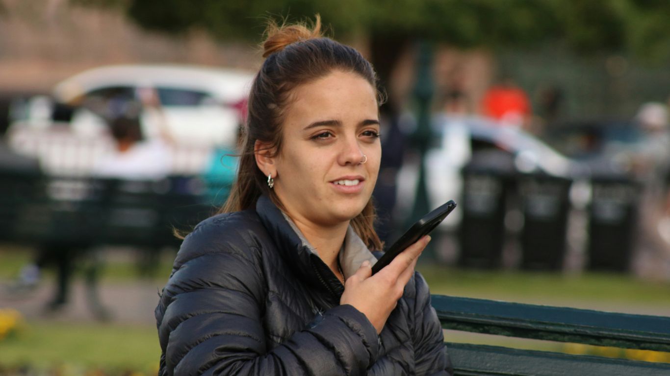 man in black bubble jacket holding smartphone while sits on bench