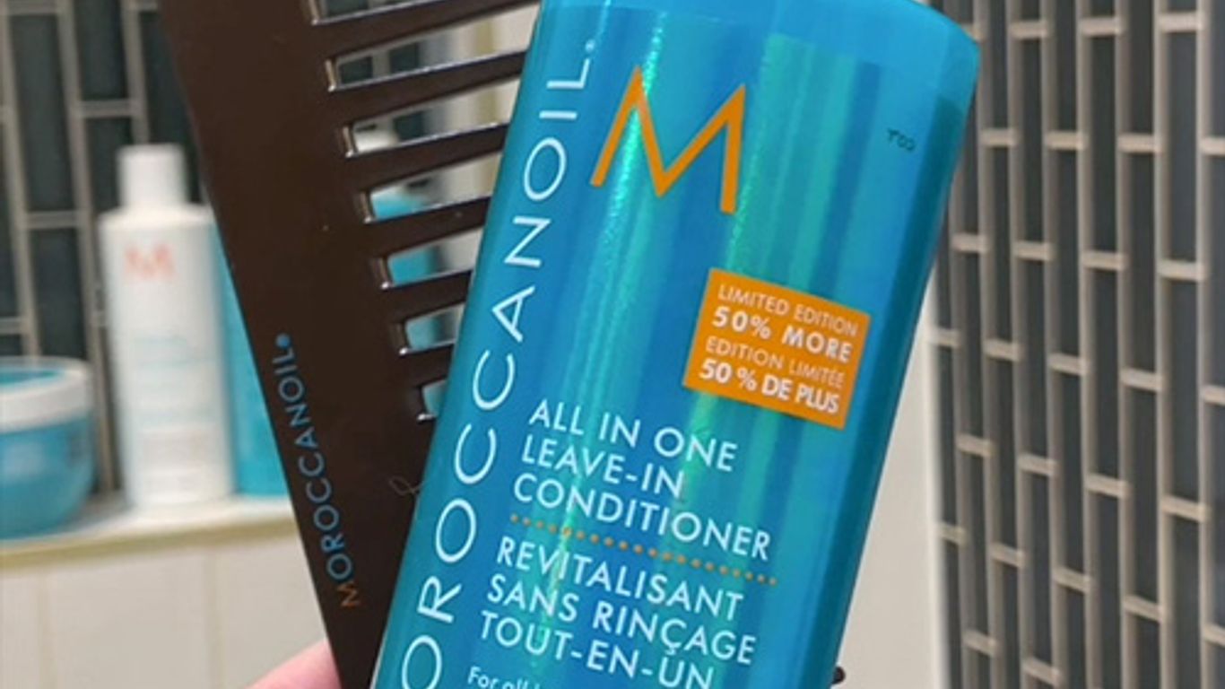 Hand holding a bottle of Moroccanoil leave-in conditioner indoors.