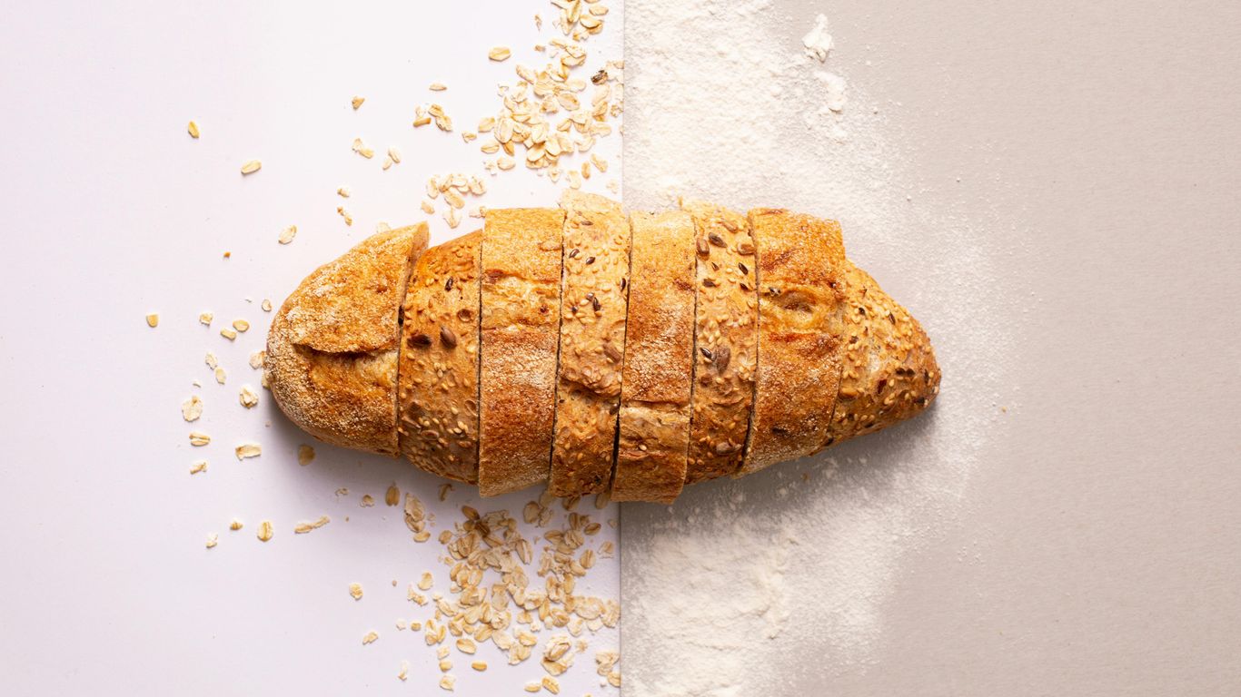 Sliced multigrain bread on split background with oats and flour.