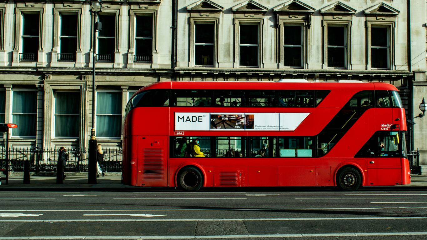a red double decker bus driving past a tall building
