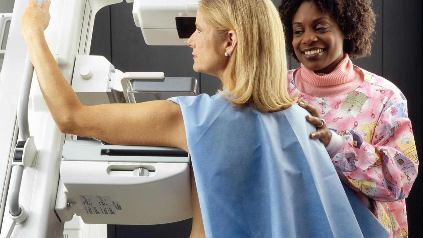 smiling woman standing near another woman beside mammogram machine