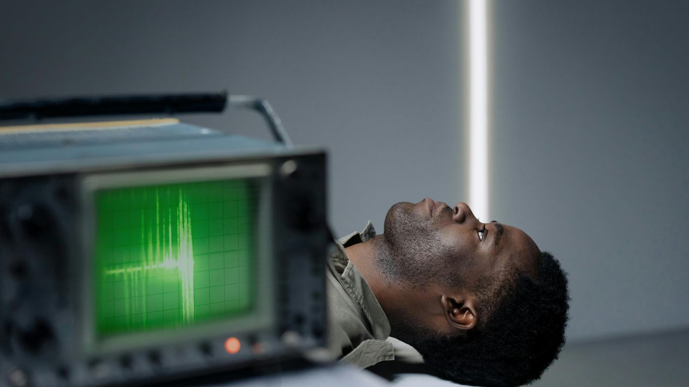 Person lying on table beside machine with green waveform display.