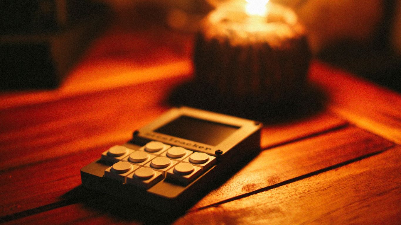 A device sits on a wooden table near a warm light.