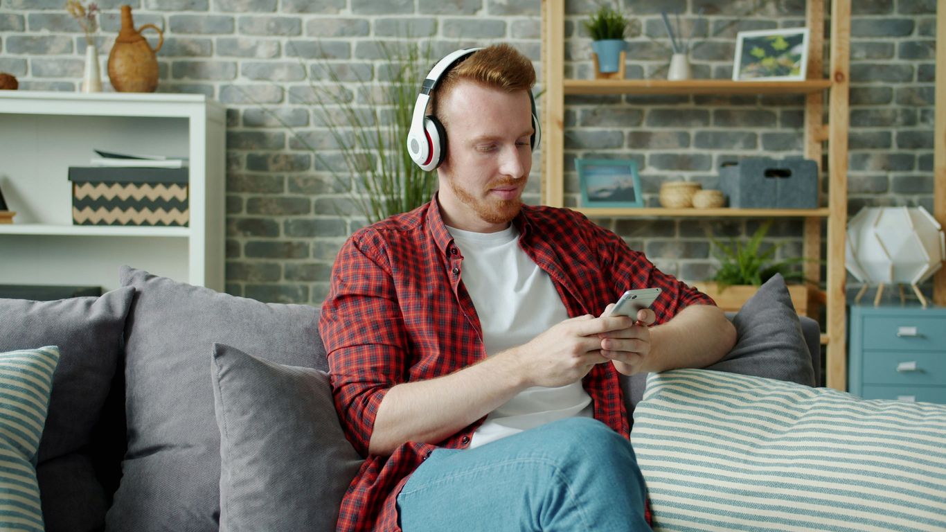 Man with headphones using phone on sofa