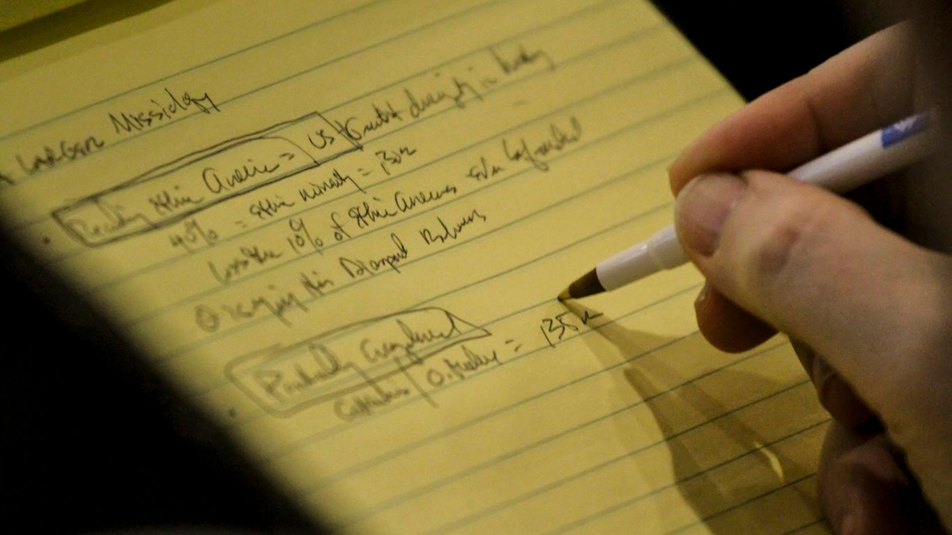 person holding white and black pen writing on yellow paper