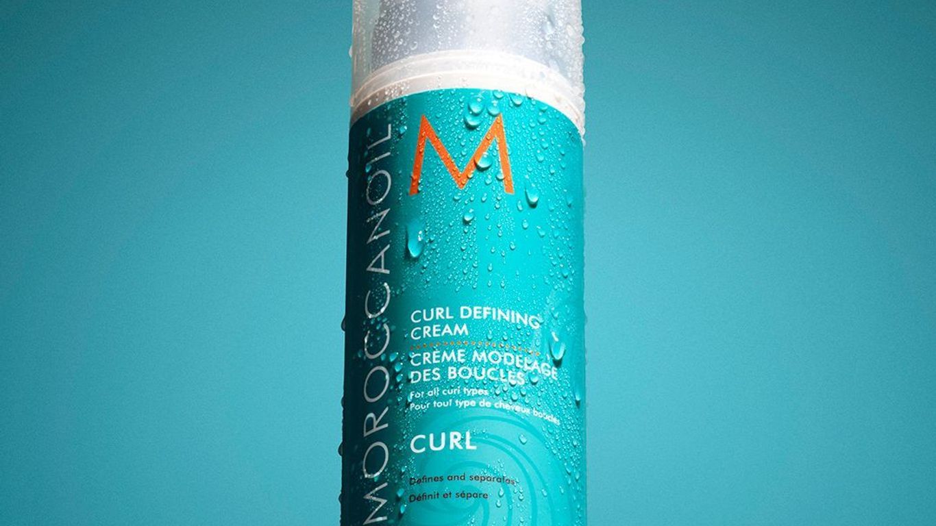 Bottle of curl-defining cream with water droplets on surface.