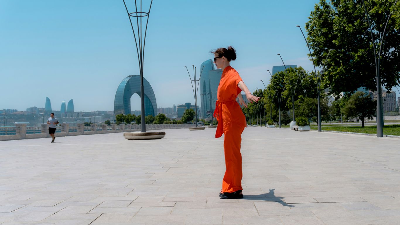 Woman in orange jumpsuit in a park with city skyline