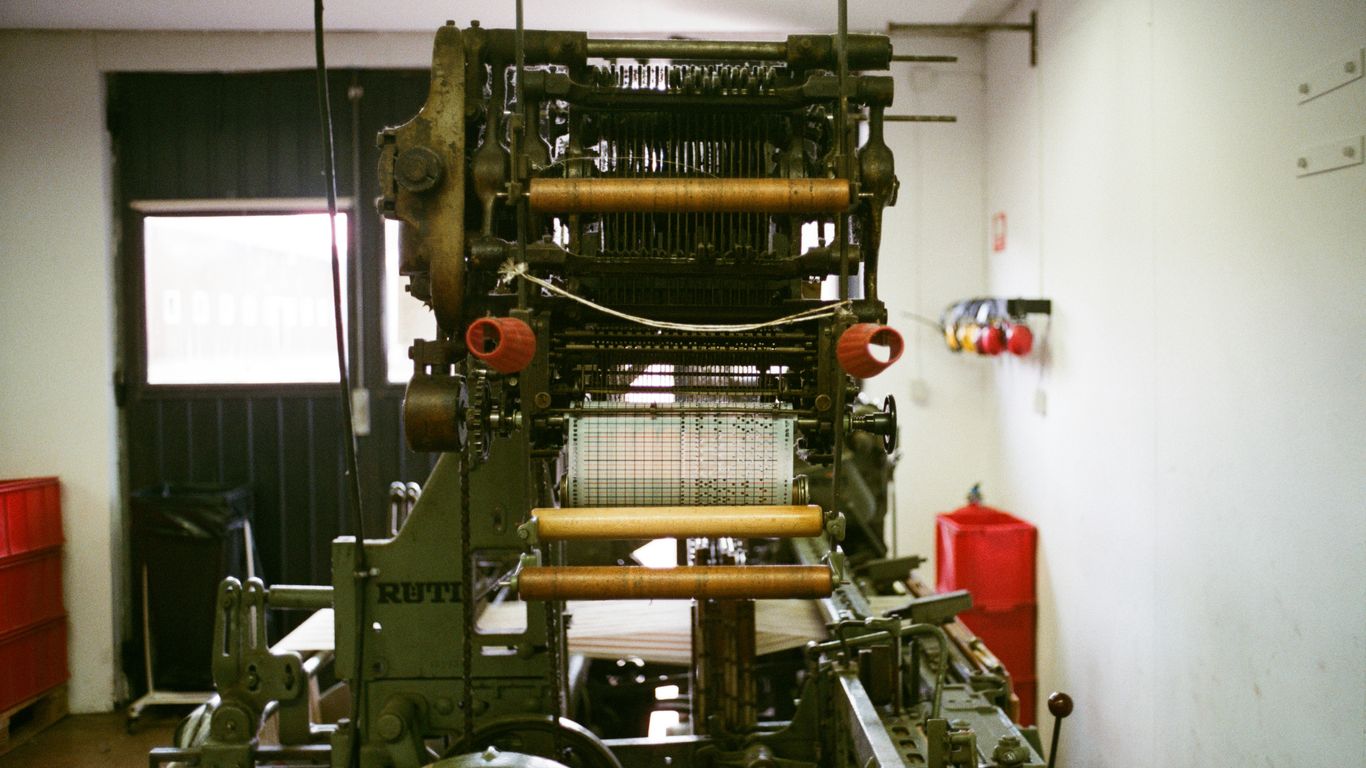 Industrial loom machine with threads and rollers.
