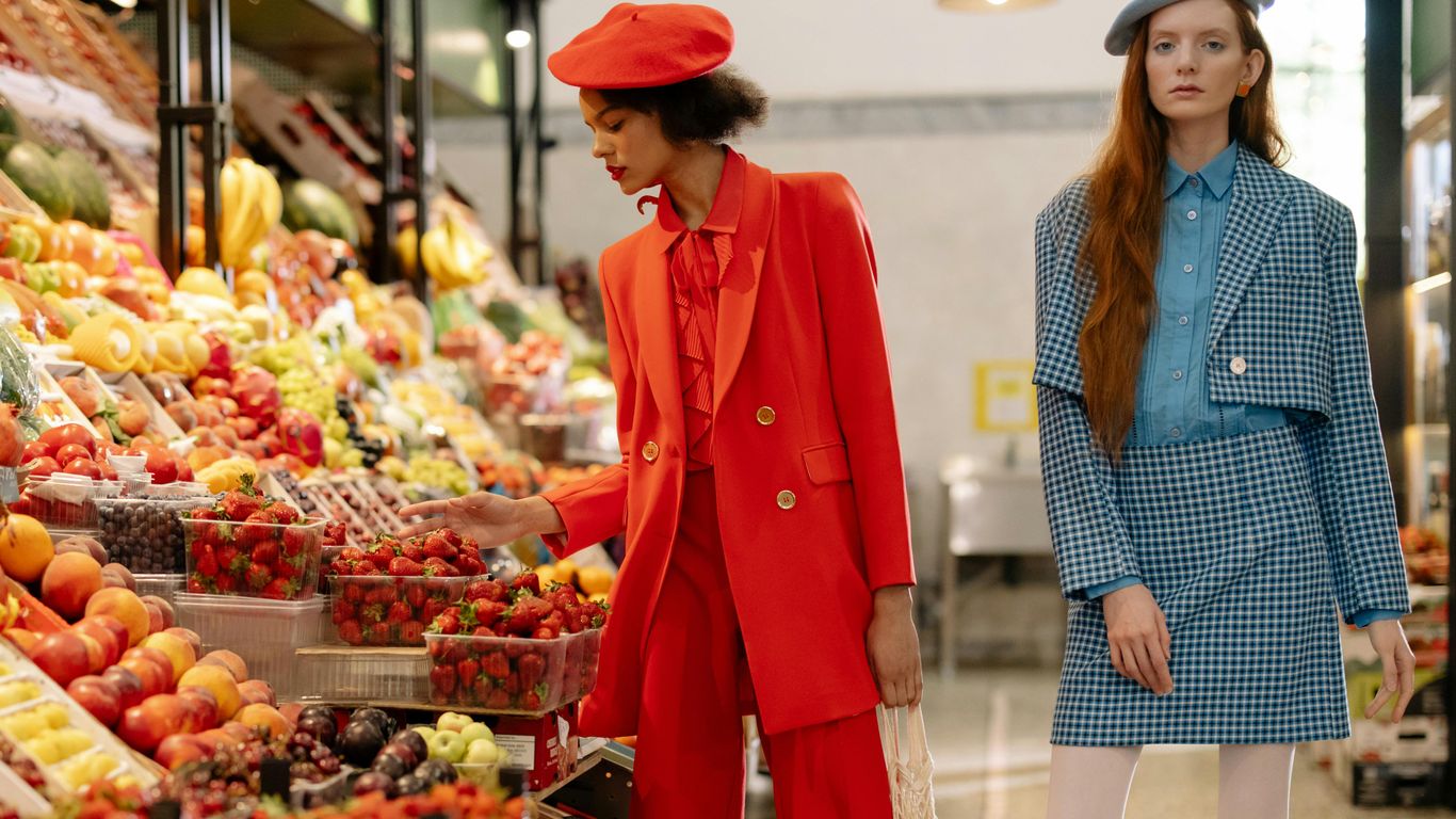Two people in stylish outfits at a vibrant fruit market.