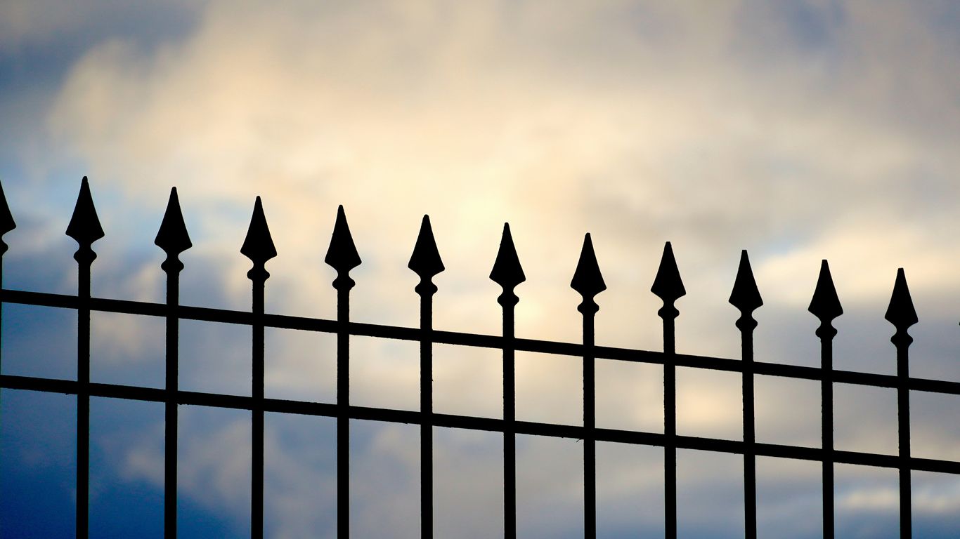 A black iron fence with a cloudy sky in the background