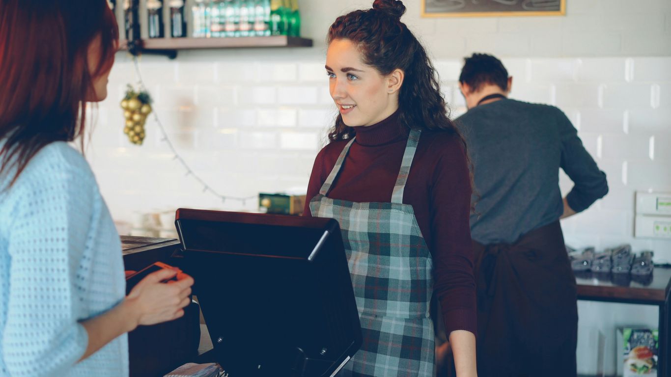 A cafe employee serves a customer at the register.