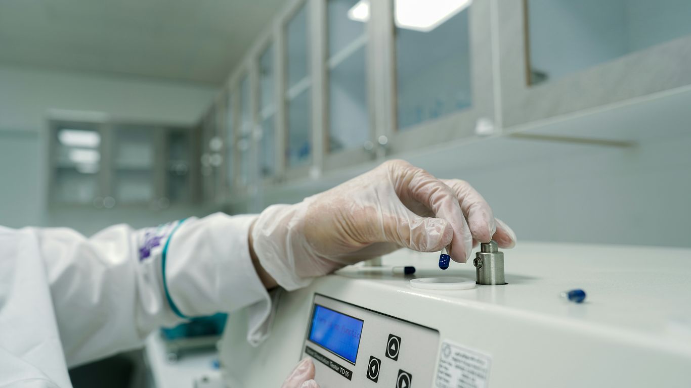 A person in a lab coat and gloves working on a machine